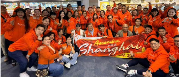 Large group of Ascenders in orange hoodies holding an Ascendra goes to Shanghai banner