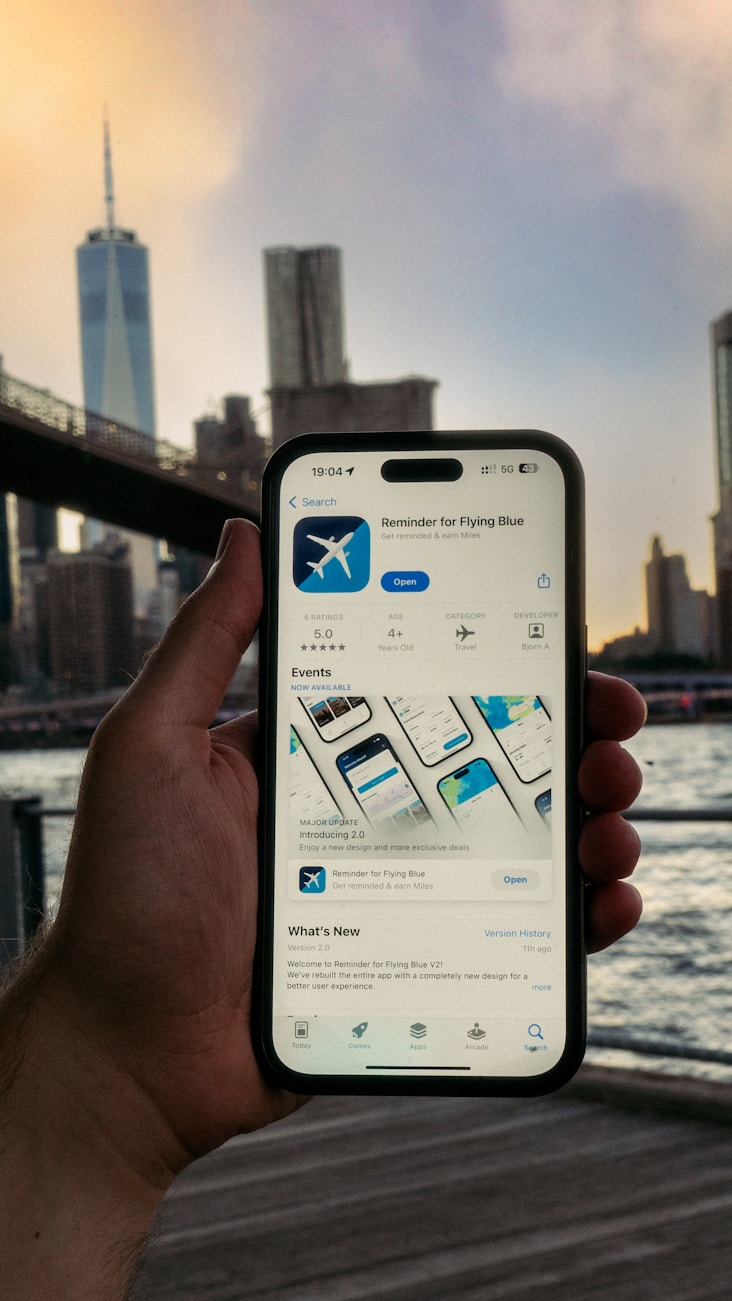 Hand holding a smartphone with an app on screen against a blurred city skyline at dusk.